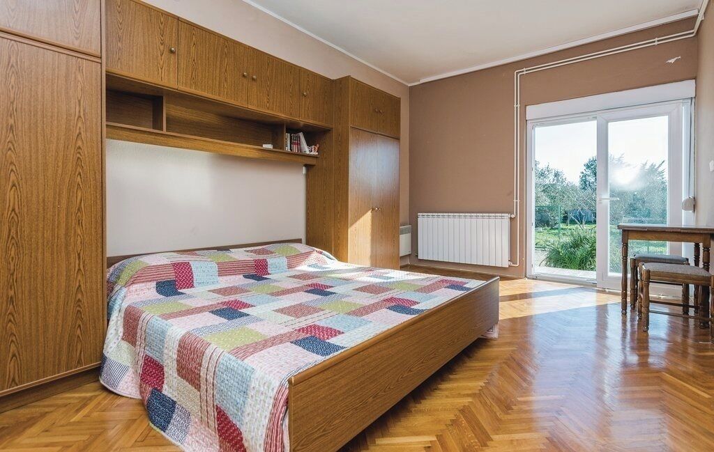 Een slaapkamer met een houten bed, ingebouwde planken en een groot raam met uitzicht op groen.