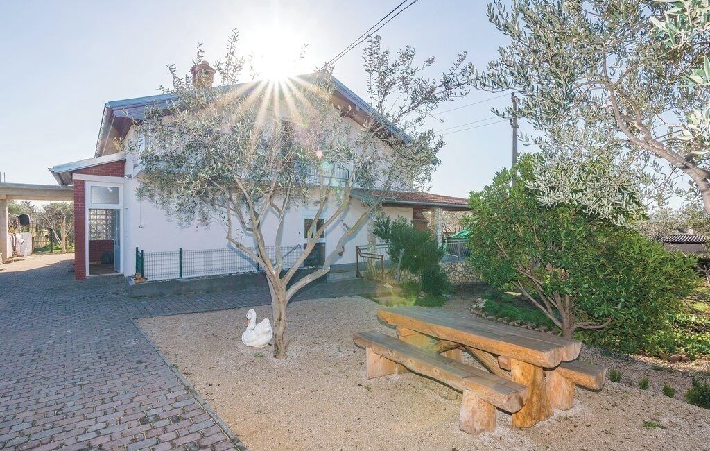 Una casa con jardín, un banco de madera y un cisne blanco.