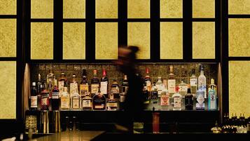 Un bar où l’on peut voir une variété de bouteilles d’alcool, et une personne qui passe devant.