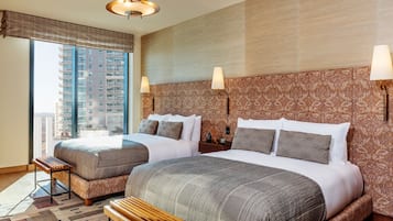 Ein Hotelzimmer mit zwei Betten, einer Bank, einem Nachttisch und einem großen Fenster mit Blick auf ein Gebäude.