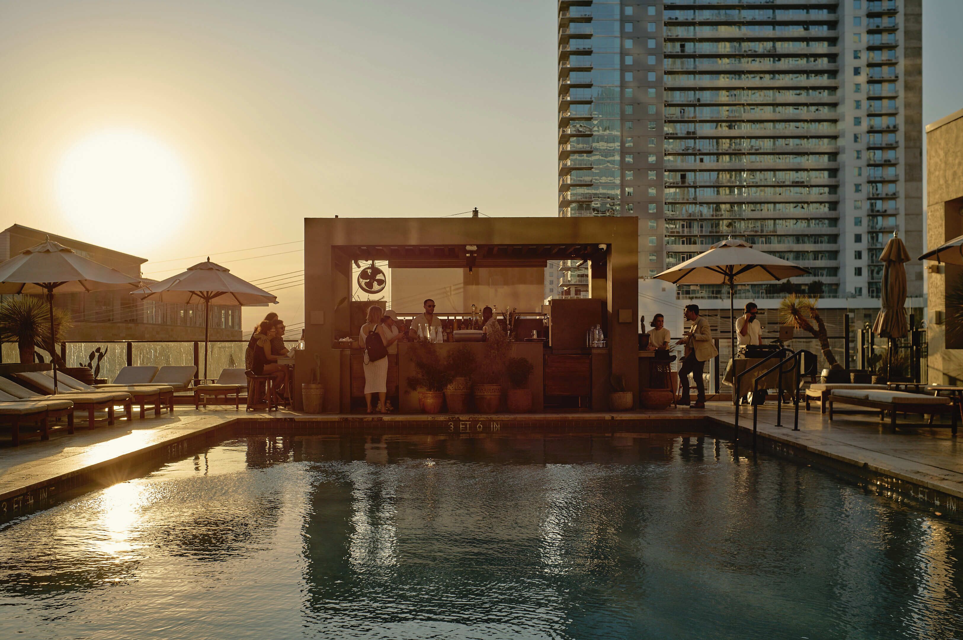A pool area with lounge chairs, umbrellas, and a bar area with people.