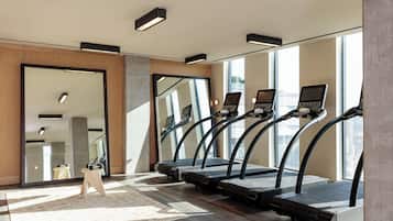Un gimnasio con cintas de correr, un espejo y un taburete de madera.
