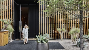 L’entrée d’un hôtel avec une façade noire, une enseigne indiquant « PROPER », et une femme qui entre.
