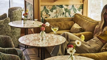 En hyggelig indretning med en sofa, to runde borde med blomsterarrangementer og en væg med blomstret tapet.