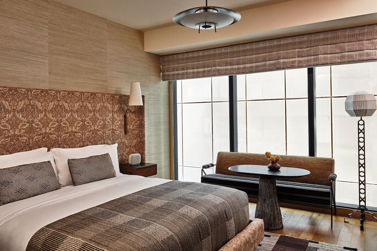 A hotel room with a large bed, a sofa, a small table, and a floor lamp.