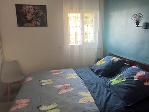 A bedroom with a bed, a chair, a wall-mounted light fixture, and a window with curtains.