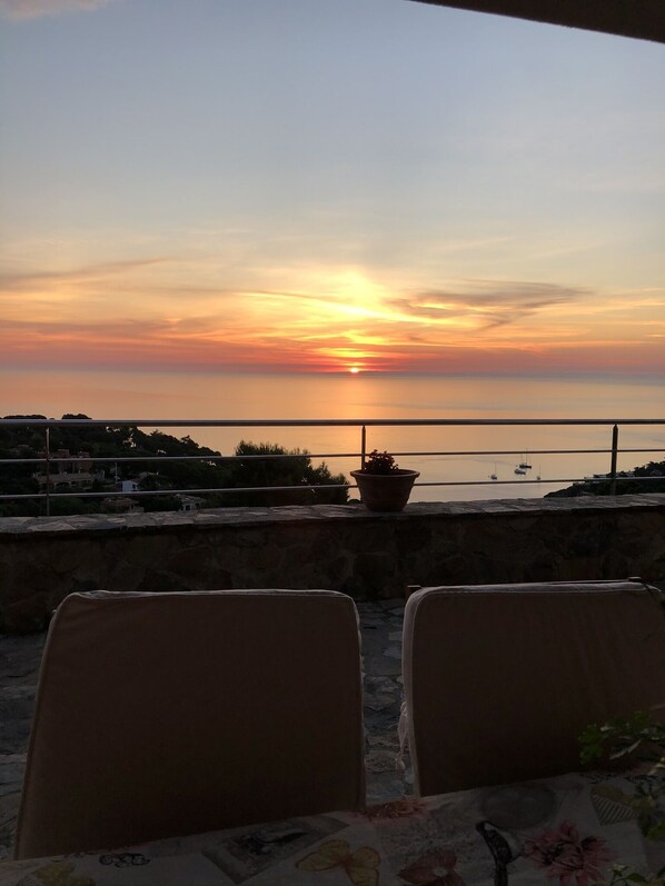 Une vue sur le coucher de soleil depuis une terrasse, avec deux chaises et une plante en pot.