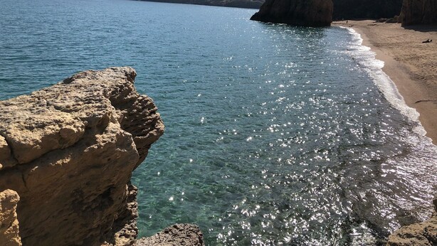 Eine Küstenlandschaft mit klarem Wasser, steinigen Klippen und einem Sandstrand.