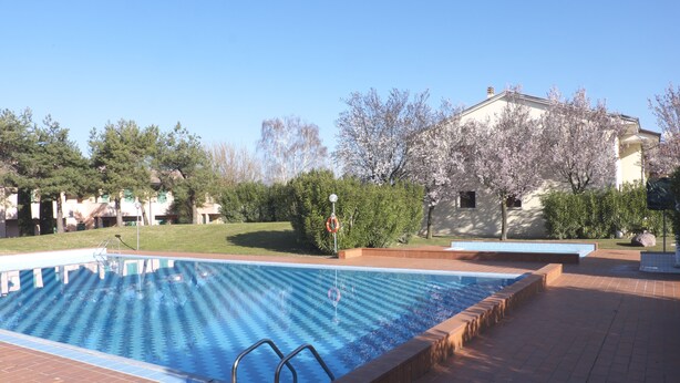 A swimming pool with a brick deck, surrounded by trees and a building. - Apartment in residence with private garden and swimming pool for adults and children and tennis (Lazise)