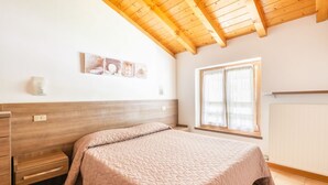 Ein Schlafzimmer mit Holzboden, einem Bett mit gesteppter Bettdecke, einem Schminktisch, einem Fenster mit Vorhängen und Wandbildern.