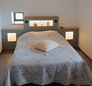A bed with a patterned bedspread and a pillow, flanked by bedside tables with built-in lighting. - Fully air-conditioned stone villa with panoramic views and private pool. (Labeaume)