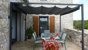 A stone building with a glass door, a covered patio with a table and chairs, and a potted plant. - Fully air-conditioned stone villa with panoramic views and private pool. (Labeaume)