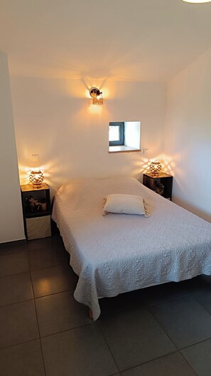 A bedroom with a bed, two bedside tables with lamps, a small window, and a wall-mounted light fixture. - Fully air-conditioned stone villa with panoramic views and private pool. (Labeaume)