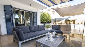 A modern outdoor living area with a grey sofa, a wooden coffee table, and a dining table. - Nirvana Seaside Villa (Pervolia)