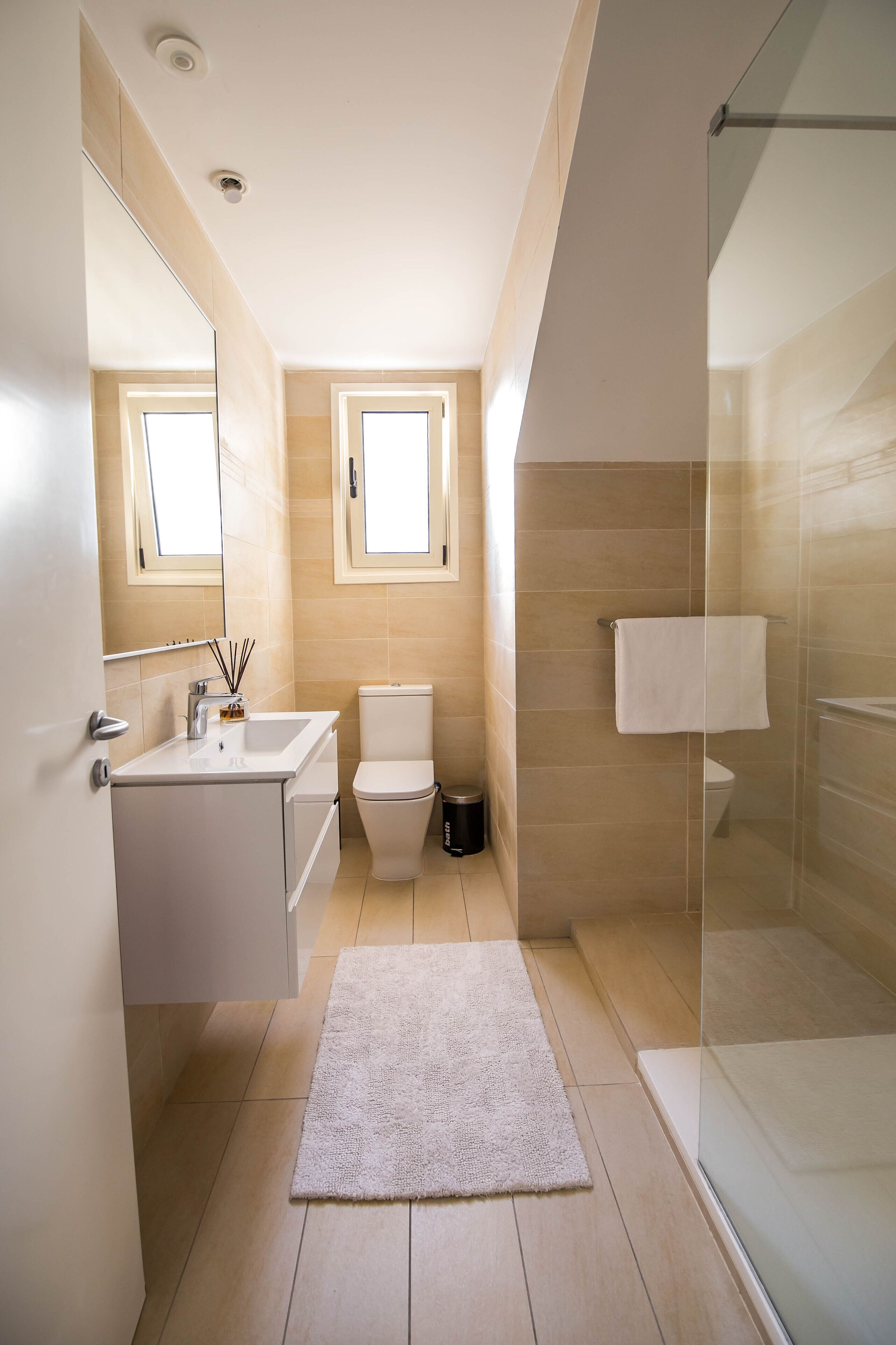 Un baño moderno con cabina de ducha de vidrio, inodoro y lavamanos con espejo.