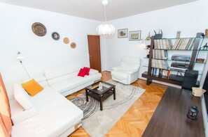 A modern living room with a white sofa, a coffee table, a white armchair, a glass bookcase, and a wooden floor.
