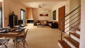 Un salon moderne comprenant un coin repas, un ensemble de canapés, un téléviseur et un escalier.