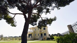 Un bâtiment à deux étages doté d’un balcon, entouré d’une pelouse bien entretenue et d’un grand arbre.