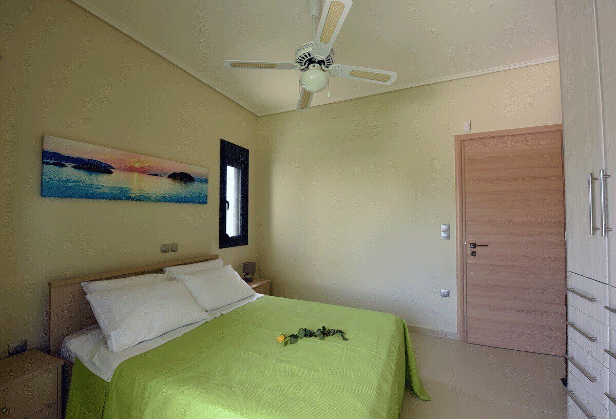 A bedroom with a bed, a ceiling fan, a painting, a window, and a door.