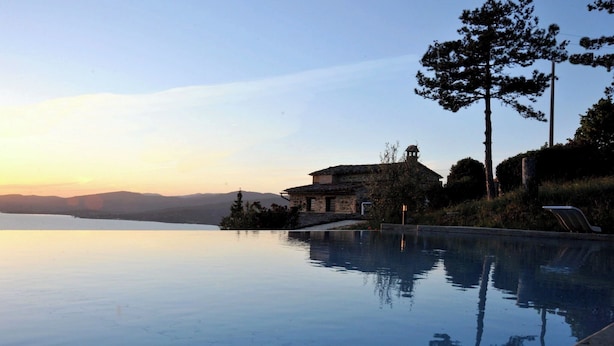Une piscine à débordement paisible, offrant une vue dégagée sur une chaîne de montagnes et, en arrière-plan, un bâtiment traditionnel en pierre.