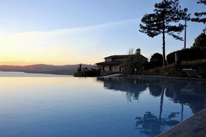 A serene infinity pool with a clear view of a mountain range and a traditional stone building in the background. - Villa Marghi, modern villa with infinity pool overlooking Lake Trasimeno (Magione)