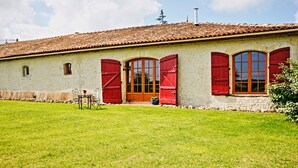 Un edificio rústico con tejado de tejas, fachada de piedra y contraventanas rojas.