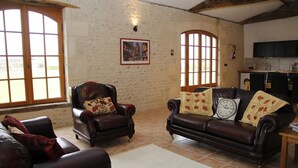 Una sala de estar con sofá y sillón de cuero, piso de baldosas y ventanas grandes.