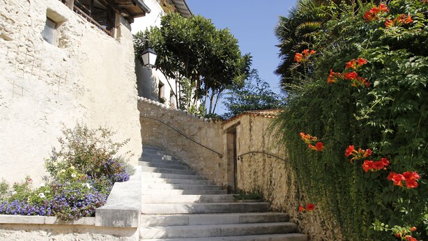 Una escalera de piedra que sube hacia un edificio de fachada blanca y una ventana pequeña.