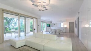 A modern living room with a sectional sofa, a dining area with a bar, and large sliding glass doors leading to a balcony. - Beautiful beach with Private Pool Villa in Castellammare del Golfo (Castellammare del Golfo)