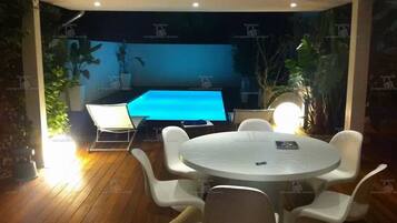 An outdoor dining area with a pool table, white chairs, and a round table.