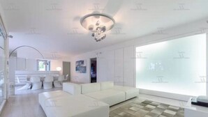 A modern living room with a white sofa, a dining area with chairs, and a large window. - Beautiful beach with Private Pool Villa in Castellammare del Golfo (Castellammare del Golfo)