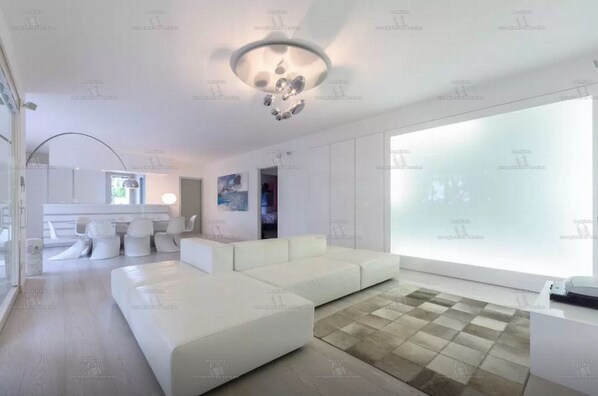 Una sala moderna con un sofá blanco, una zona de comedor con sillas y un ventanal grande.