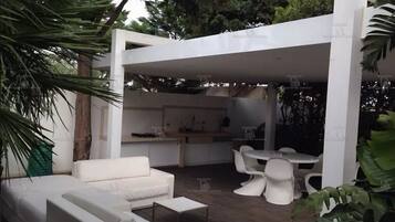 Un patio al aire libre con un sofá blanco, una mesa de comedor y sillas.