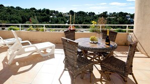 Une terrasse avec des chaises en osier, une table ronde et une bouteille de champagne.