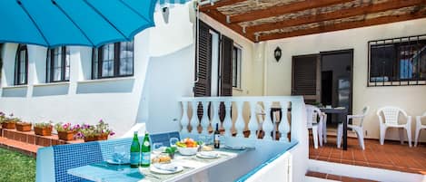 Eine Terrasse mit Esstisch für zwei Personen, einem blauen Sonnenschirm und Topfpflanzen.
