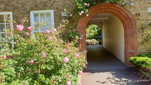 A brick archway leading to a pathway, surrounded by blooming pink roses and greenery. - Fabulous one double bedroom flat in garden setting by the river in Battersea (London)