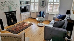 A living room with a fireplace, sofa, armchair, and a glass coffee table. - Fabulous one double bedroom flat in garden setting by the river in Battersea (London)