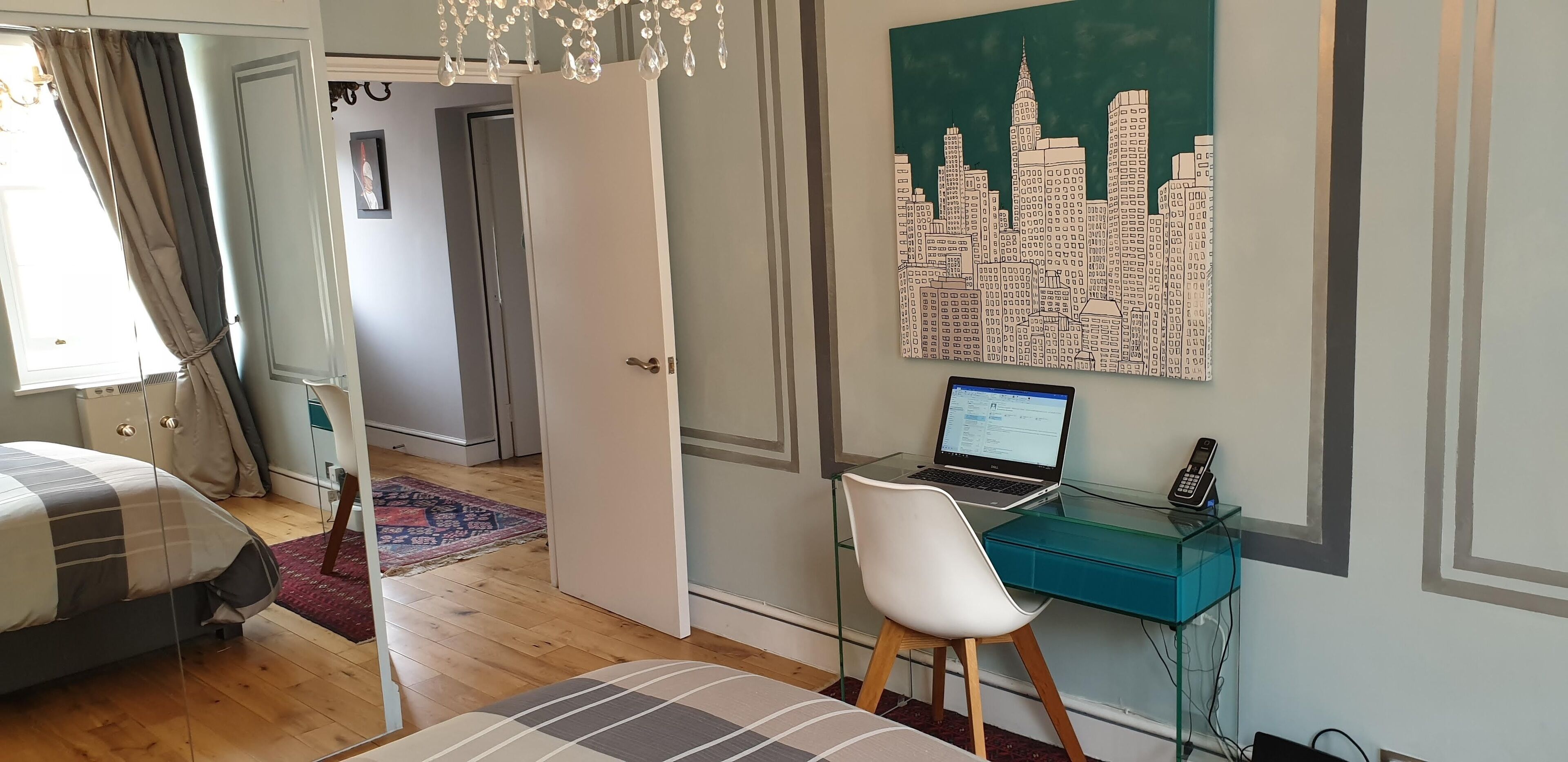 Ein Schlafzimmer mit Bett, Schreibtisch mit Laptop und Stadtbild an der Wand.