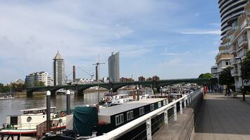 A riverside walkway with a bridge, boats, and buildings in the background.