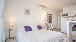A bedroom with a bed, a chair, a desk, a microwave, and an air conditioning unit.