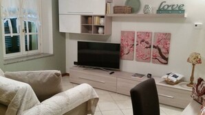 A living room with a TV, a sofa, a cabinet, and a window with curtains.