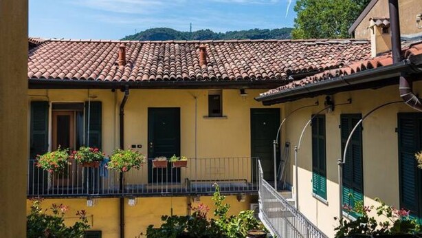 A yellow building with a tiled roof, balconies with railings, and potted plants.