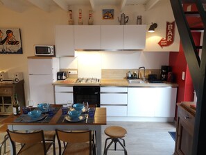 Cocina moderna con gabinetes blancos, estufa a gas y un lavamanos. Hay una mesa de comedor con cuencos azules y copas de vino.