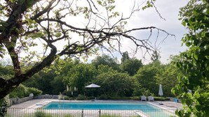 A rectangular swimming pool with a metal fence, surrounded by lush greenery and trees. - Characterful Farmhouse And Large Pool in Rural Setting, sleeps 10 (Lusignac)