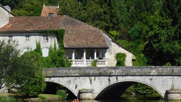A stone bridge over a river with a building on the left. - Characterful Farmhouse And Large Pool in Rural Setting, sleeps 10 (Lusignac)