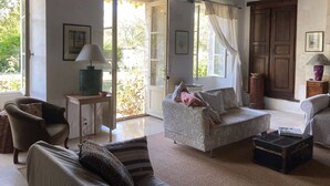 A cozy room with a wooden ceiling, a sofa, a chair, a small table with a lamp, and a window with curtains. - Characterful Farmhouse And Large Pool in Rural Setting, sleeps 10 (Lusignac)