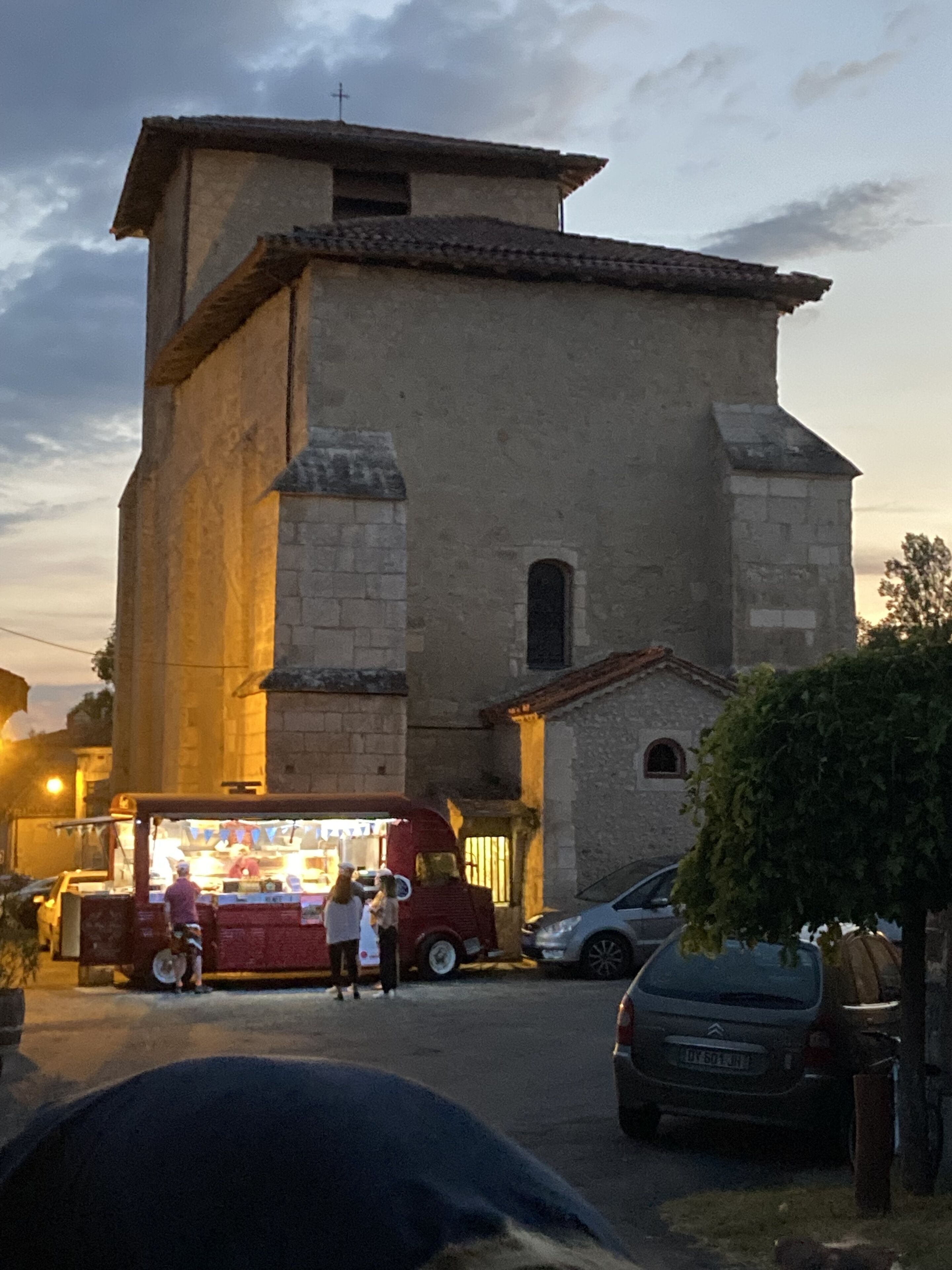 Un bâtiment à la façade en pierre, une petite construction attenante avec un toit en tuiles et une voiture garée devant.