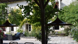 An outdoor patio area with tables and chairs, surrounded by greenery and a stone wall. - Characterful Farmhouse And Large Pool in Rural Setting, sleeps 10 (Lusignac)