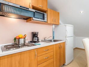 A compact kitchen with wooden cabinets, a built-in microwave, a coffee maker, and a refrigerator.