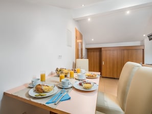 Una mesa de desayuno dispuesta con platos, tazas y vasos, una silla y una puerta de madera al fondo.